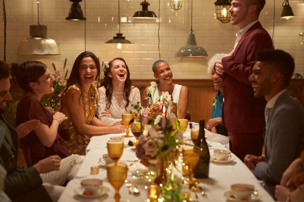 Two married girls having fun at their dinner party with their close friends as they listen to the best mans speech.