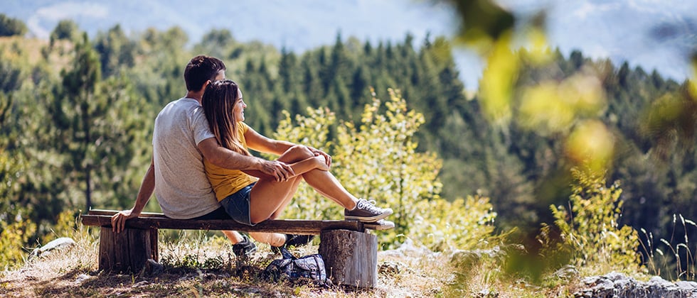 Young couple sitting on bench and enjoying in the beautiful view, on summer day as example for day date idea