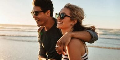Man and woman laughing together on the beach as a symbol of healthy relationship characteristics