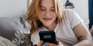 Woman lying in bed and smiling at her mobile phone as a symbol for online dating tips