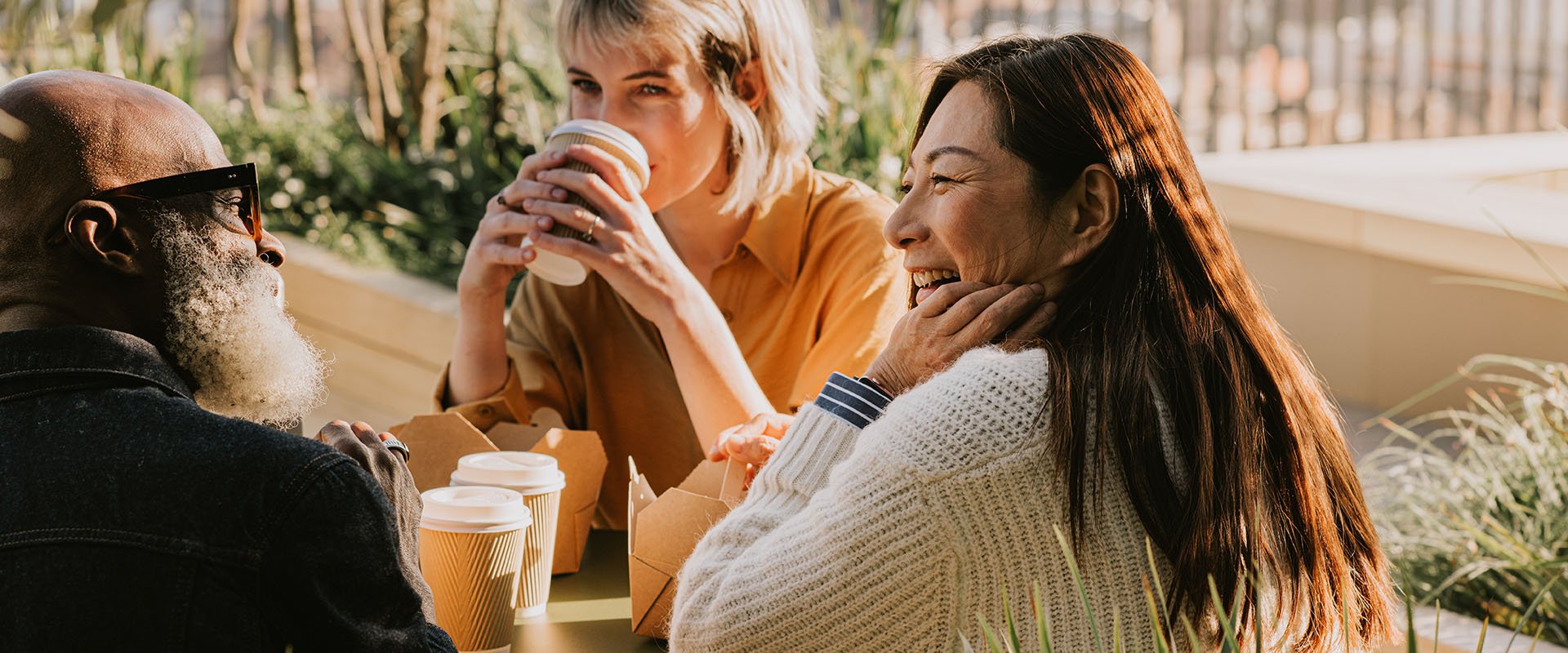 Two women and a man are sitting together with coffees and snacks. They are laughing and seem to have a good time together.