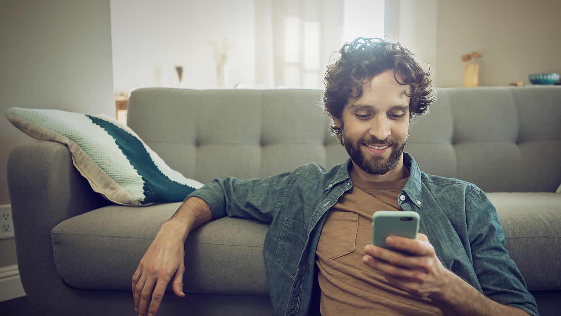 Man with cell phone in hand on the sofa informs himself about tips for eharmony settings