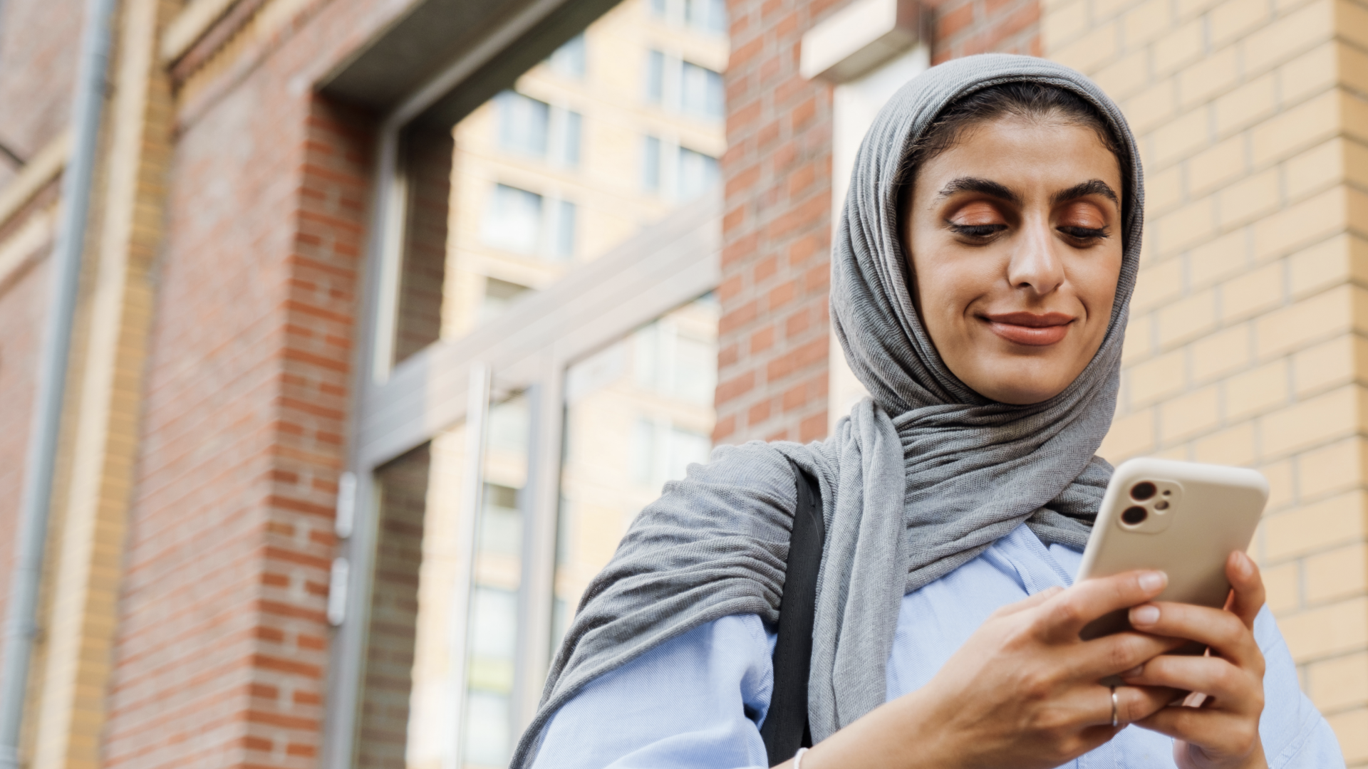 A woman looks at her cell phone and smiles, symbolizing Muslim dating