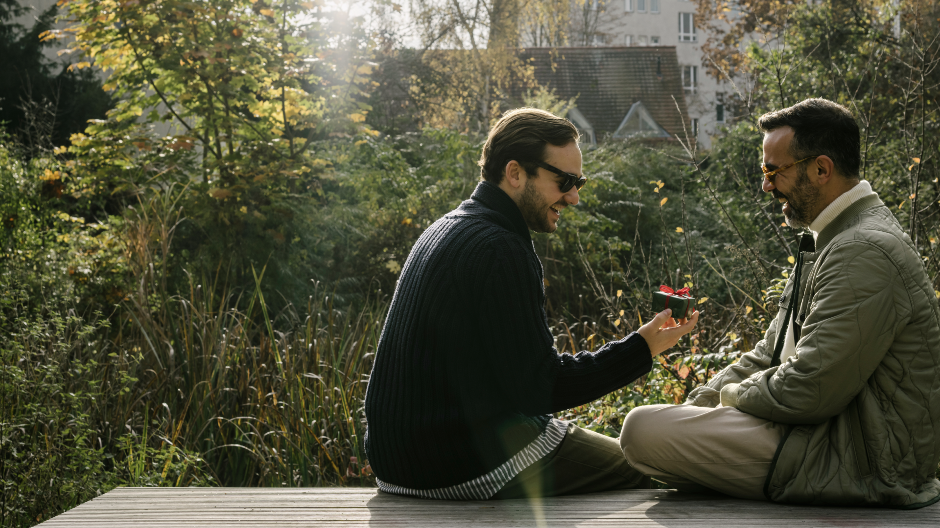 Two men are sitting outside, laughing together—a symbol of gay dating
