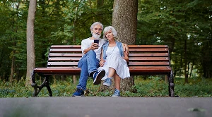 A couple are sitting on a bench in a park, chatting.