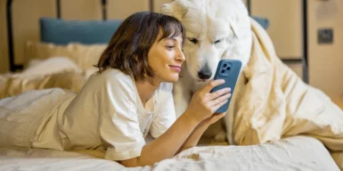 Woman sitting with her dog on the bed and looking to her phone.