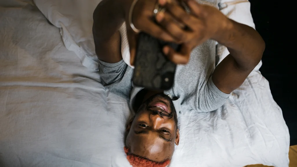 A man is lying on the bed looking at his phone.