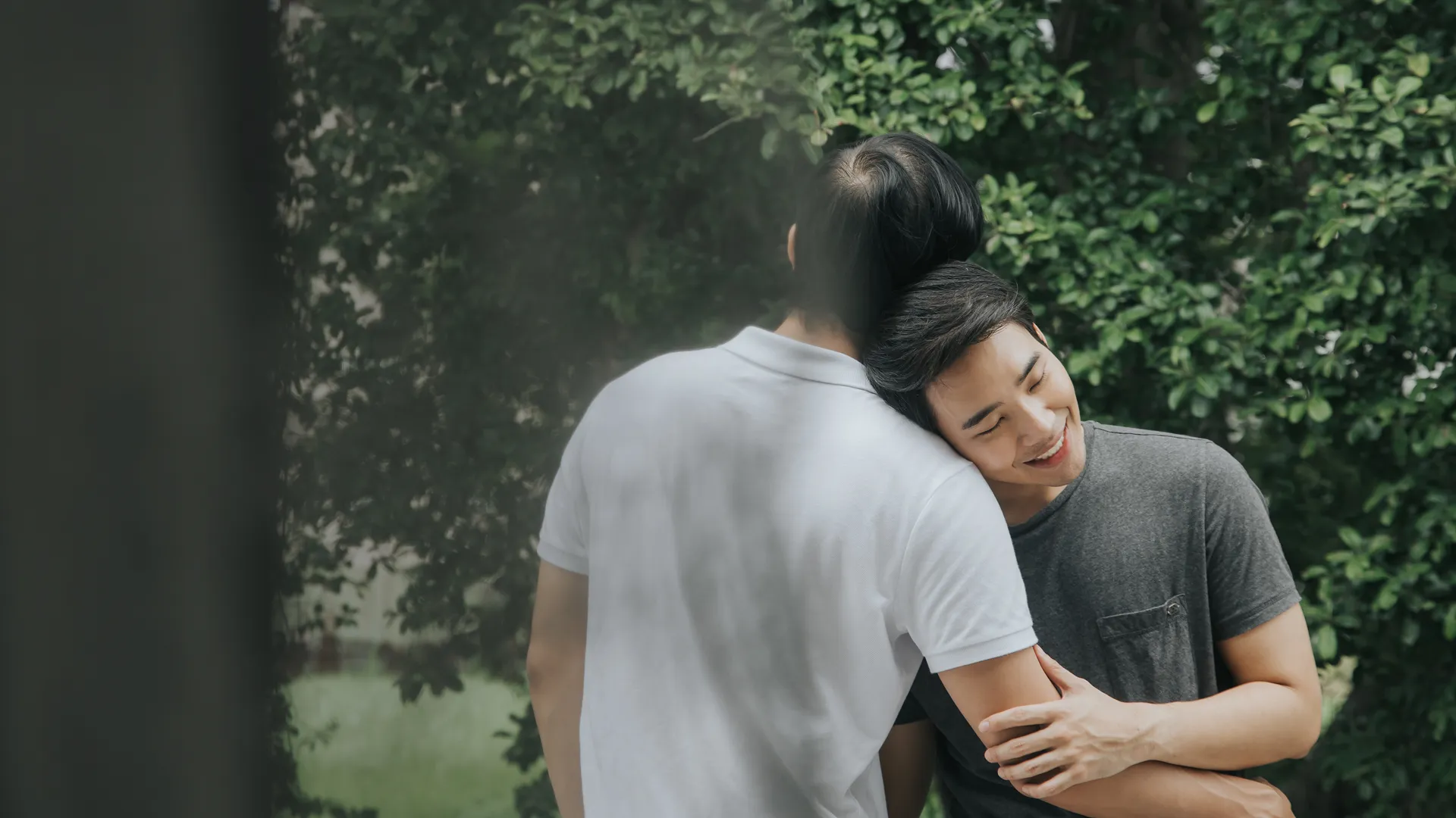 A gay Korean couple are hugging each other in the backyard.