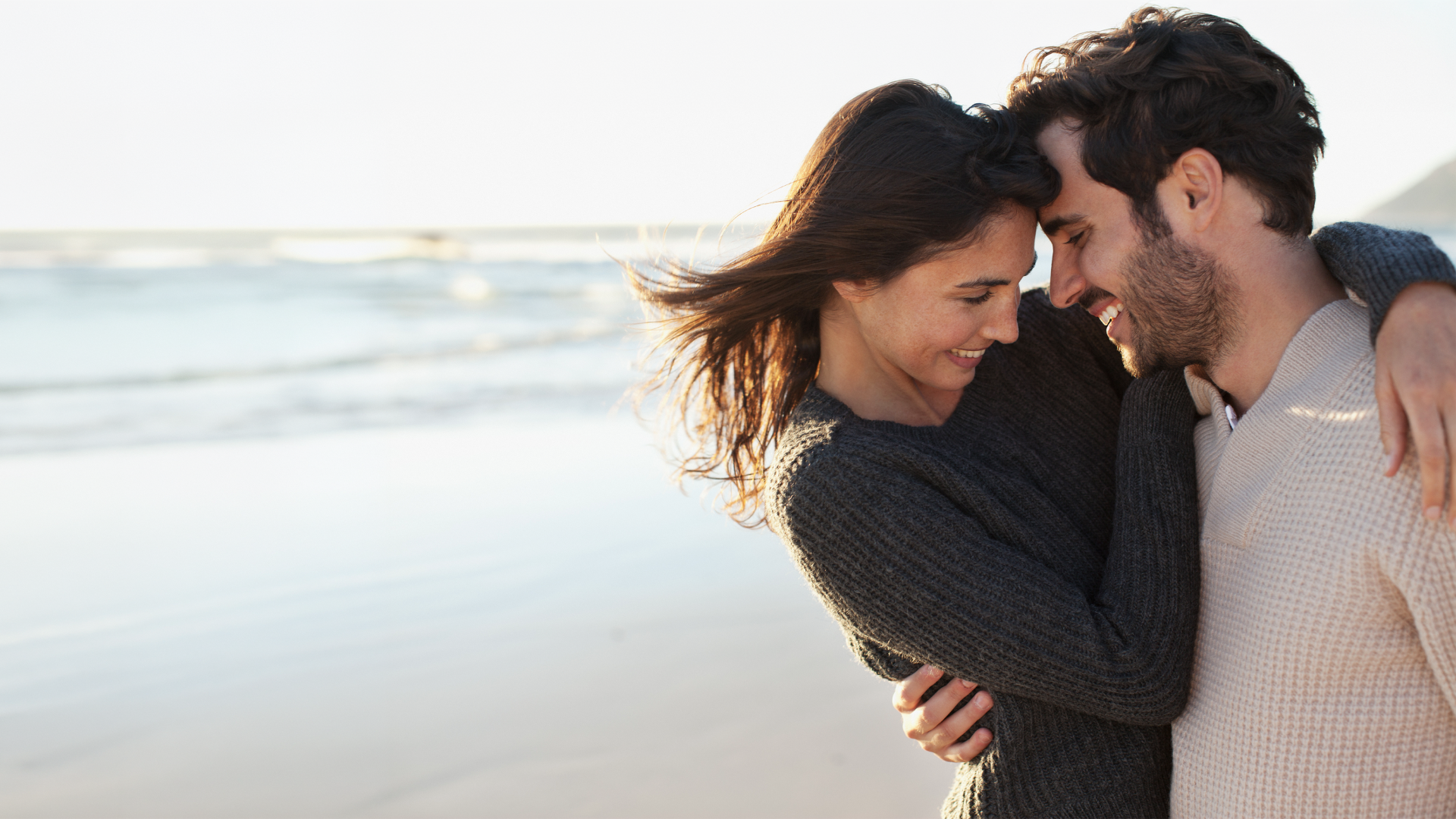 A man and a woman embrace on the beach as a symbol of eharmony