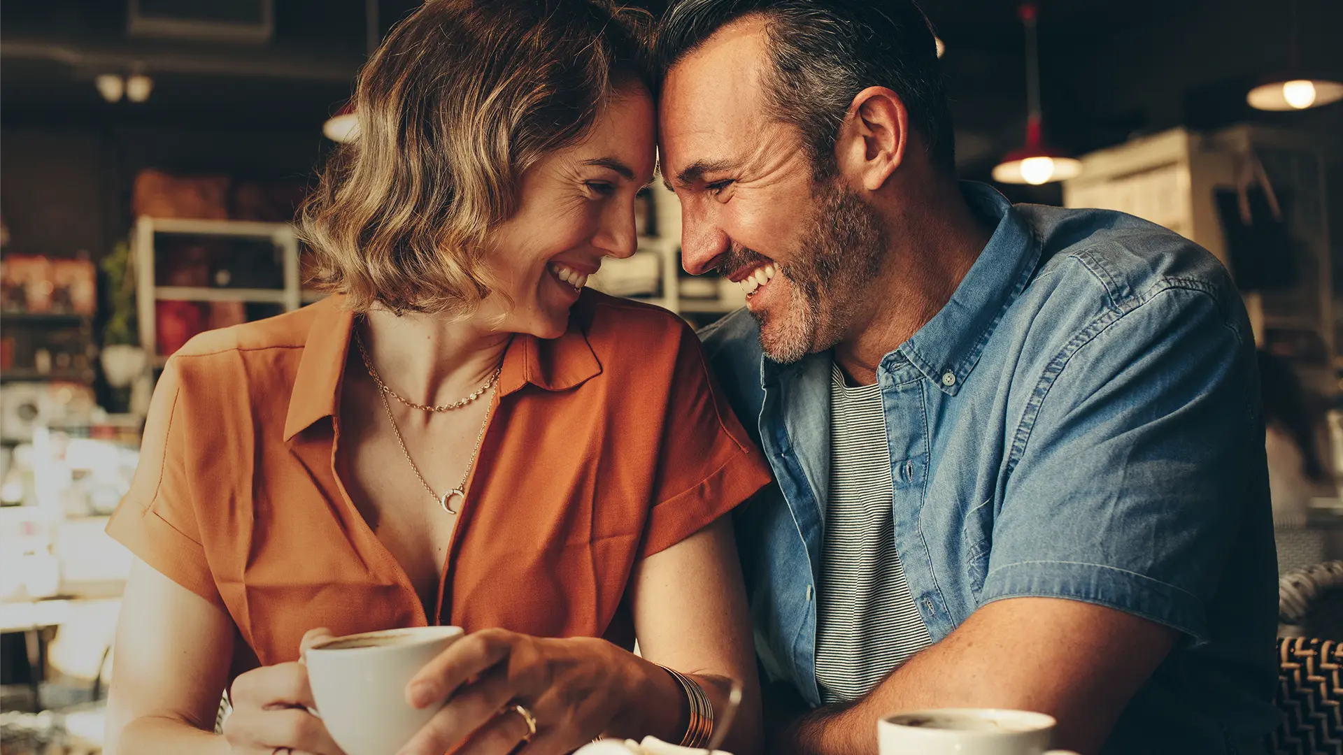 A couple in their 40s on a date laughing and looking at each other.